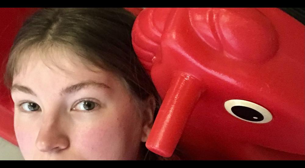 A close-up of someone lying against a red plastic rocking horse