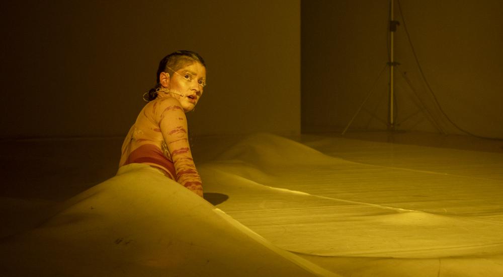 A dancer lying on the floor half-tucked under some kind of plastic sheet
