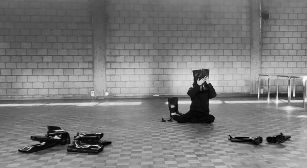 A person sitting on the floor holding two boots in front of their face, while others are scattered over the floor