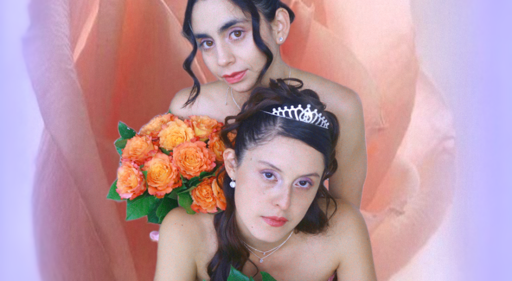 Estefania and Luisa wearing tiaras and carrying flowers in front of a flower background