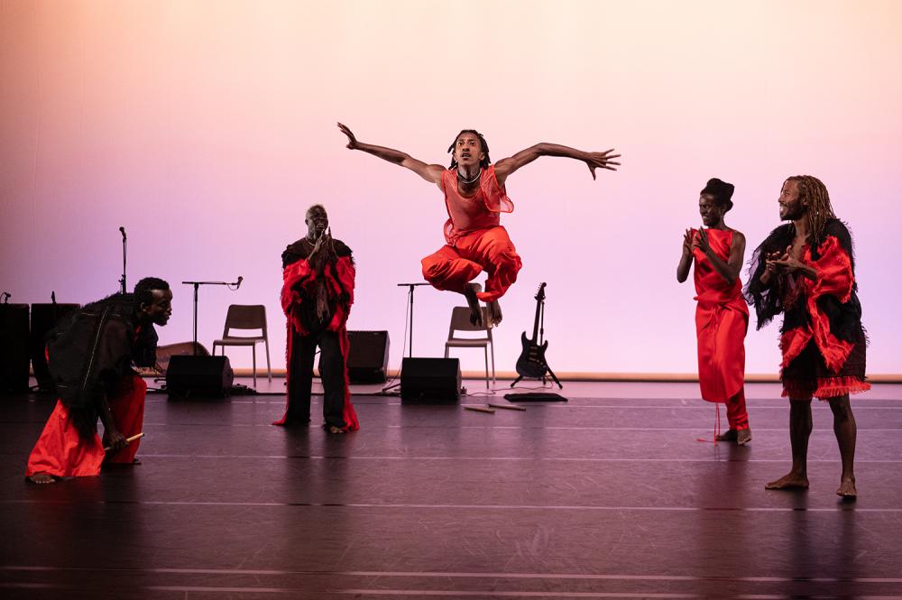 4 dancers standing around one jumping in the air