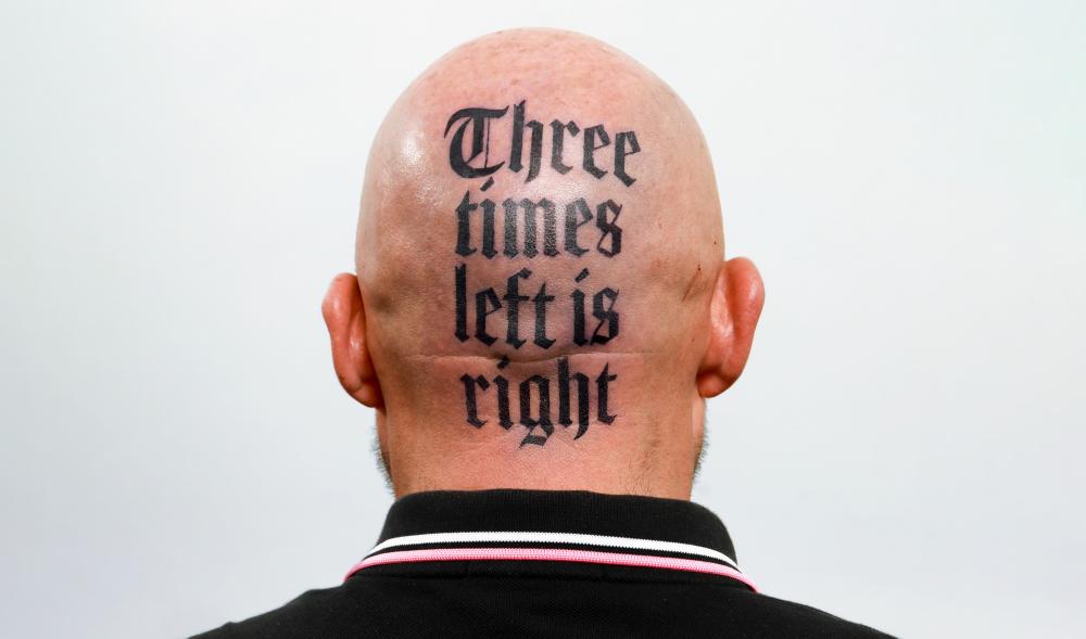 The back of bald person's head with a tattoo that reads "Three times left is right"