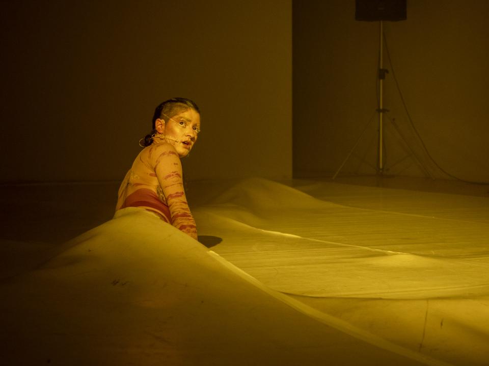 A dancer lying on the floor half-tucked under some kind of plastic sheet