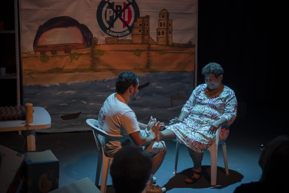 Anacarsis and his mother sitting on chairs facing each other on stage