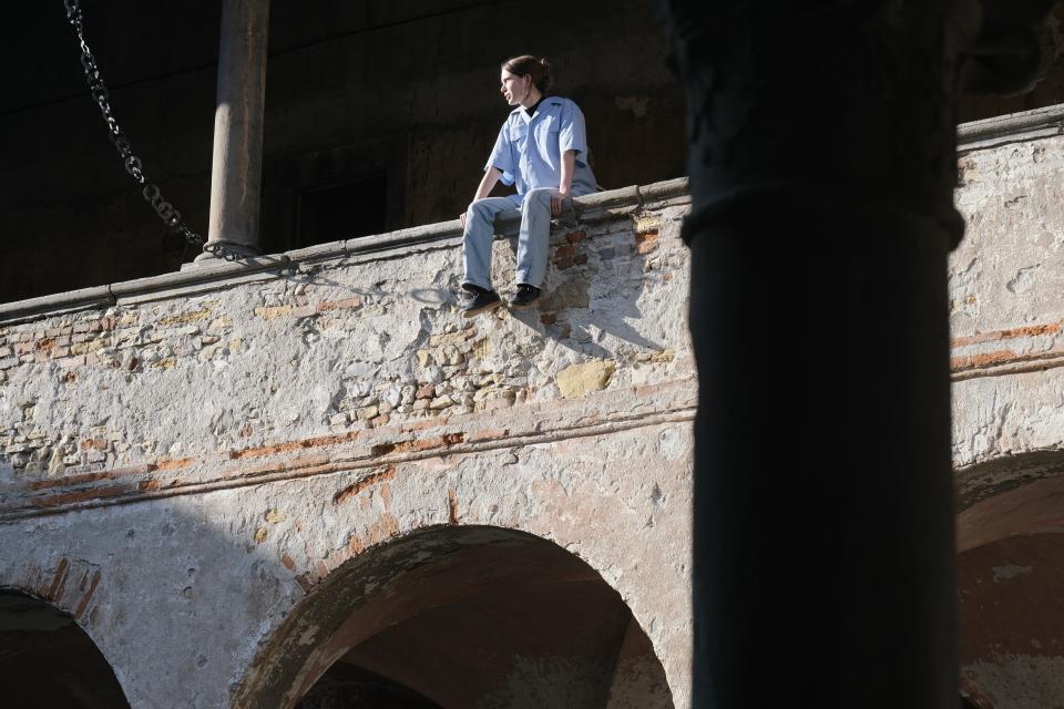 A young person sitting on the ledge of an old brick wall