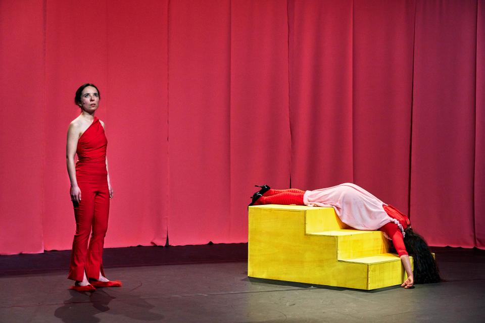 one performer in front of a red curtain, the other one is laying on yellow stairs