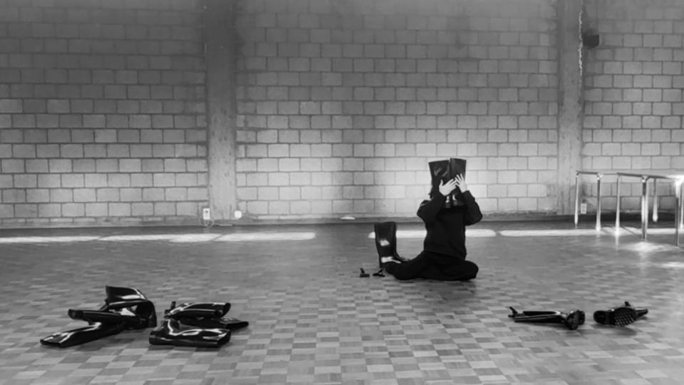 A person sitting on the floor holding two boots in front of their face, while others are scattered over the floor