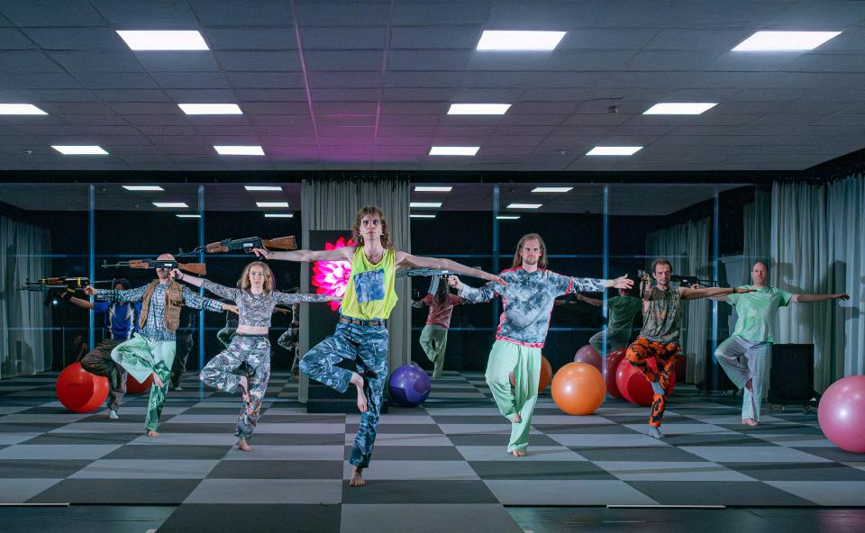 A group of people wearing colourful clothes in a yoga studio with exercise balls. Some of them are holding machine guns
