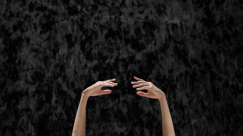 Two hands in a ballet pose in front of a black background