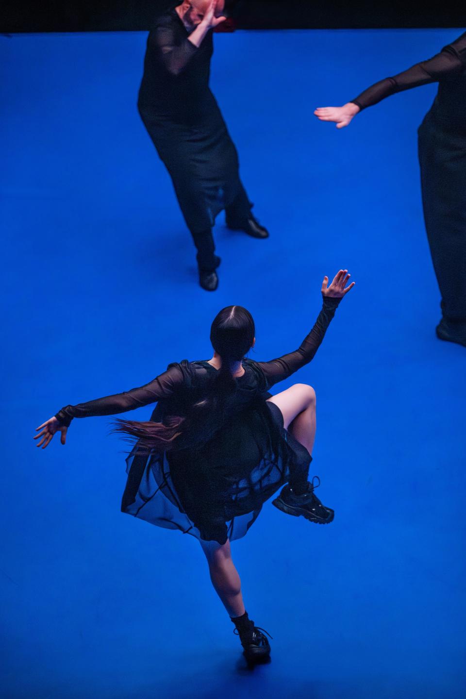3 performers with black clothes dancing on a bright blue floor